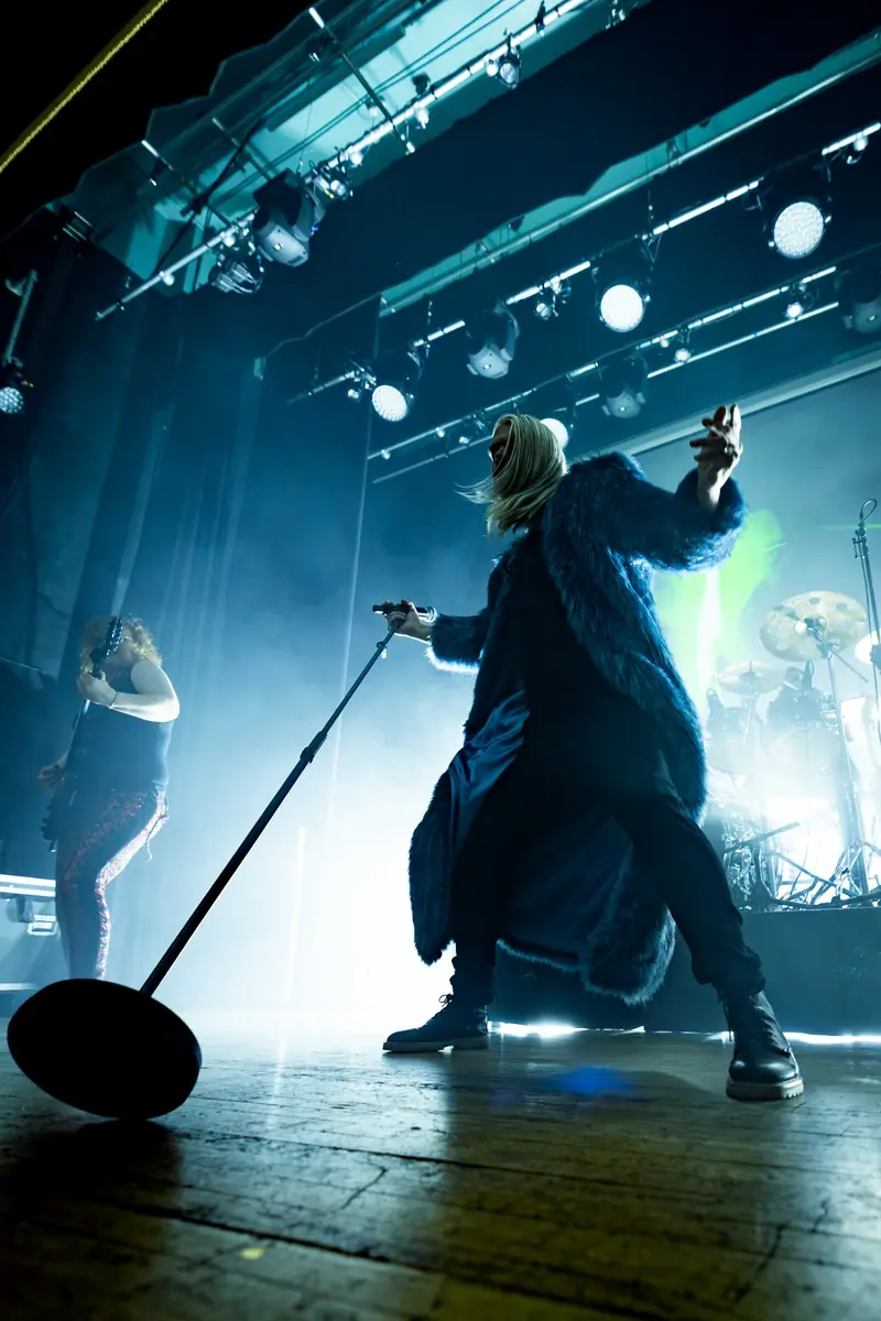 Voyager - Islington Assembly Hall London - 31 July 2026 Photo Ryan HildrewMetalTalk | MetalTalk - Heavy Metal News Reviews and Interviews Lead singer in a blue faux-fur coat performs center stage with a tilted microphone stand, smoke and blue lights.